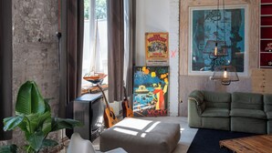 A room with a brick wall, a television, a guitar, a sofa, and a painting. - STORAGE LOFT APARTMENT URBAN (Berlin)