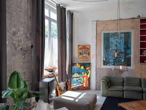 Ein Zimmer mit Backsteinwand, Fernseher, Gitarre, Sofa und einem Gemälde.