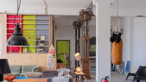 A room with a wooden table, chairs, a sofa, a colorful shelf, a lamp, and a fire extinguisher. - STORAGE LOFT APARTMENT URBAN (Berlin)