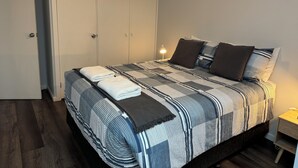 A neatly made bed with a striped bedspread and pillows, a bedside lamp, and a wardrobe with a door. - 2 Bedroom Apartment located in the heart of Ulladulla. (Ulladulla)