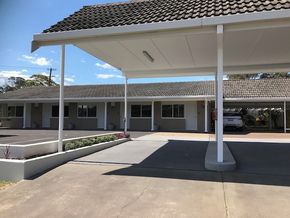 A motel with a covered parking area, a white exterior, and a tiled roof.