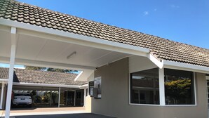 A building with a tiled roof, a covered parking area, and a large window.