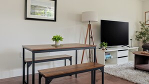 Ett vardagsrum med en tv, en inramad tavla, en lampa och ett litet bord med en växt.