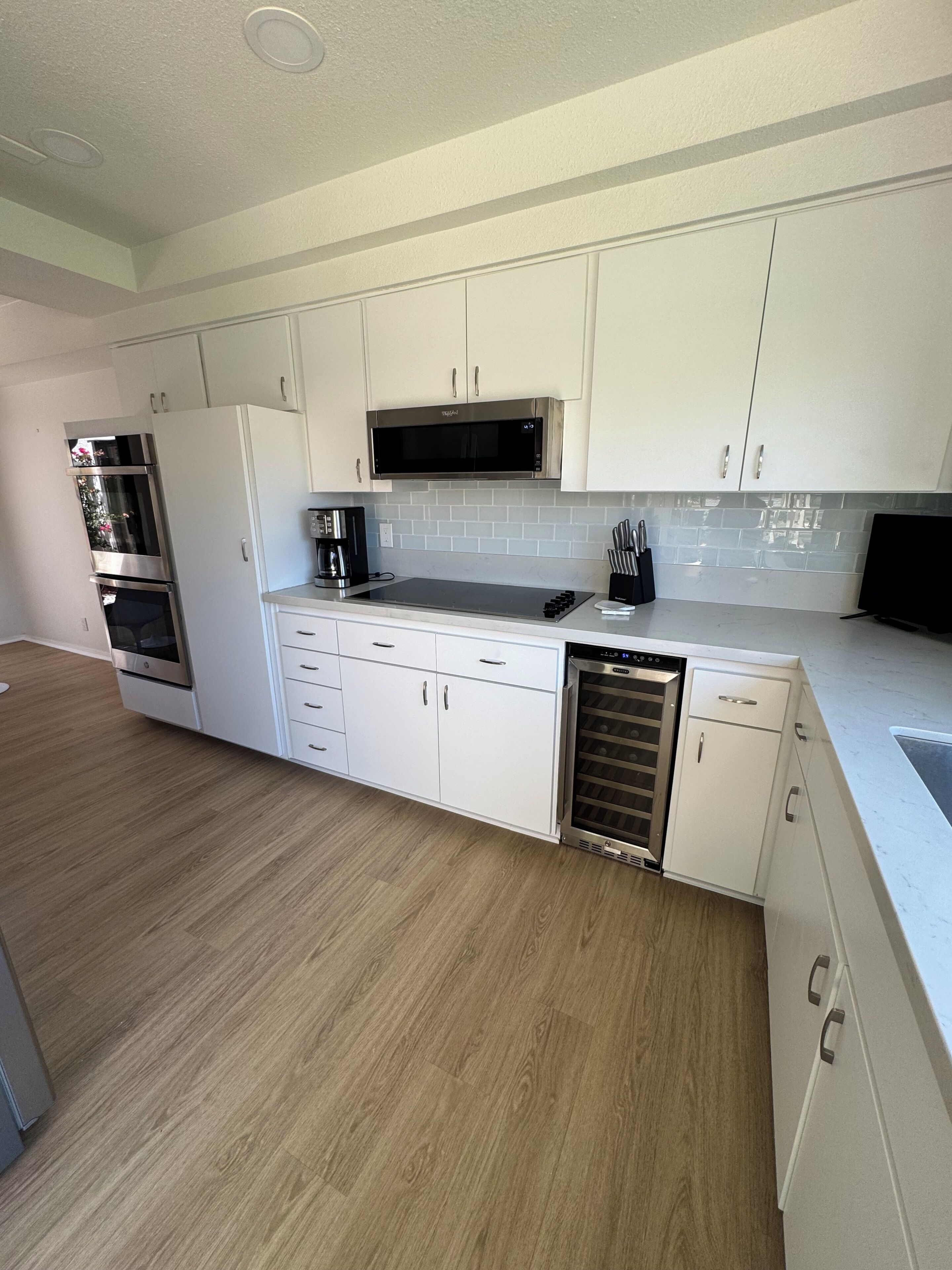 A modern kitchen with white cabinets, stainless steel appliances, a tiled backsplash, and a wooden floor.