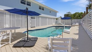 A pool area with a white deck, lounge chairs, and umbrellas.