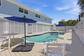 A pool area with a white deck, lounge chairs, and umbrellas.