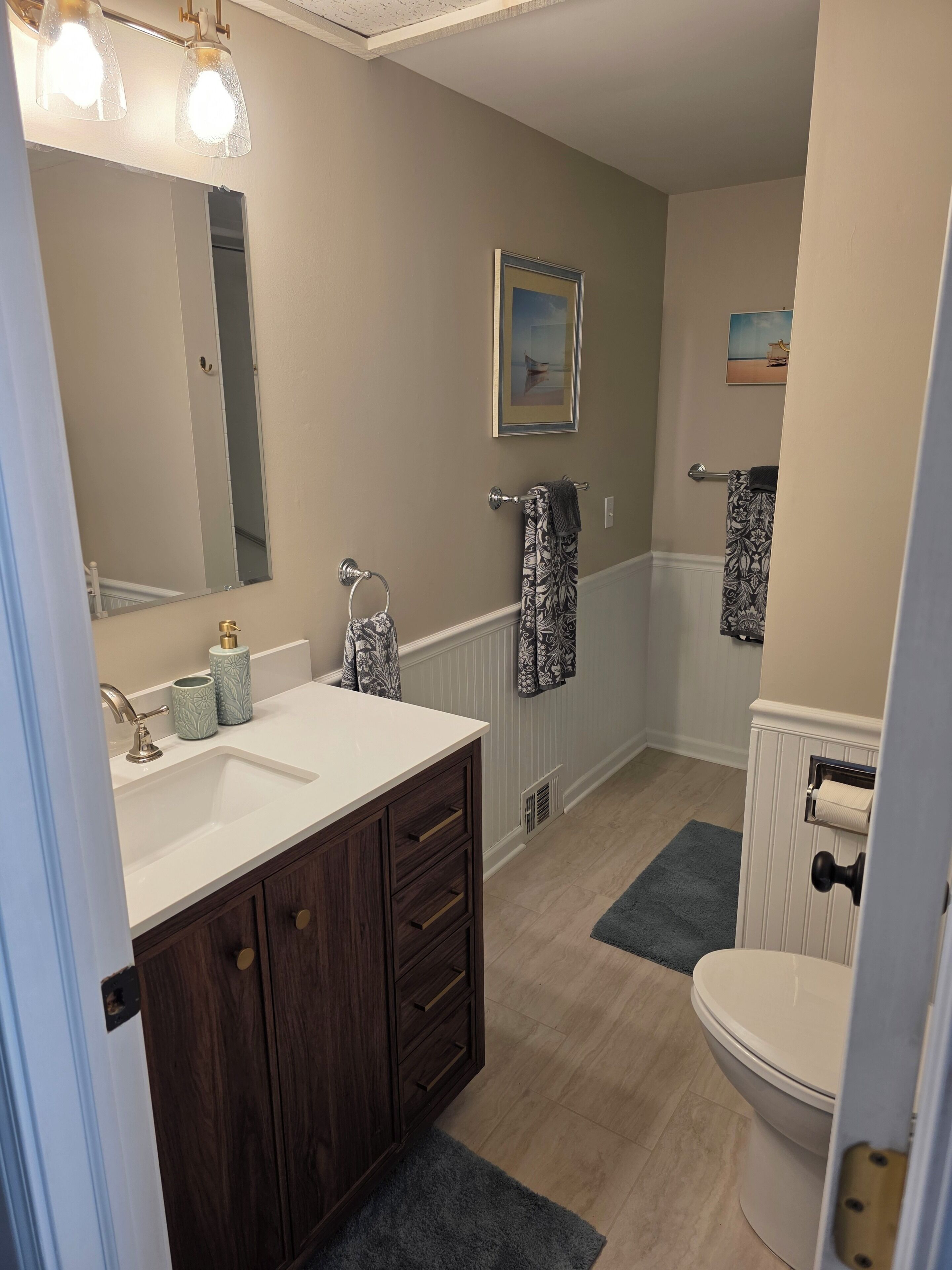A bathroom with a white sink, dark wooden vanity, a toilet, and a shower area.