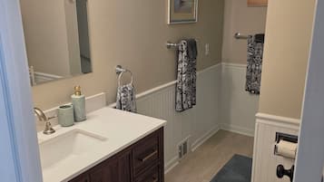 A bathroom with a white sink, dark wooden vanity, a toilet, and a shower area.