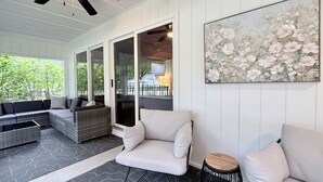 Une terrasse couverte avec un ventilateur au plafond, des meubles en osier et un grand tableau représentant des motifs floraux.