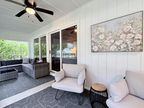 Eine überdachte Terrasse mit Deckenventilator, Korbmöbeln und einem großen Blumenbild.