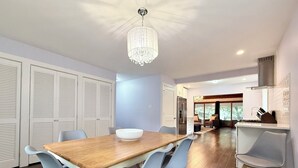 Un espace repas moderne avec une table en bois, des chaises bleues, un lustre et une vue sur le salon.