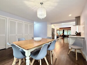 Ein moderner Essbereich mit einem Holztisch, blauen Stühlen, einer Chandelierleuchte und Blick in ein Wohnzimmer.