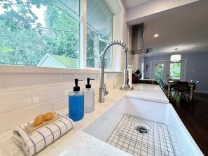 A modern kitchen with a large window, a stainless steel sink, and a dining area visible through the window. - Whimsy Wild: Walk to Downtown Saugatuck, Sauna, Hot Tub, Screen Porch, Fire Pit (Saugatuck)