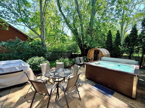 Une terrasse extérieure avec un jacuzzi, un barbecue couvert et une table ronde avec des chaises.