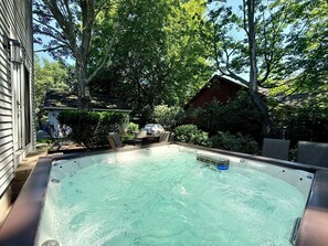Un bain à remous dans un jardin, avec une maison et des arbres en arrière-plan.