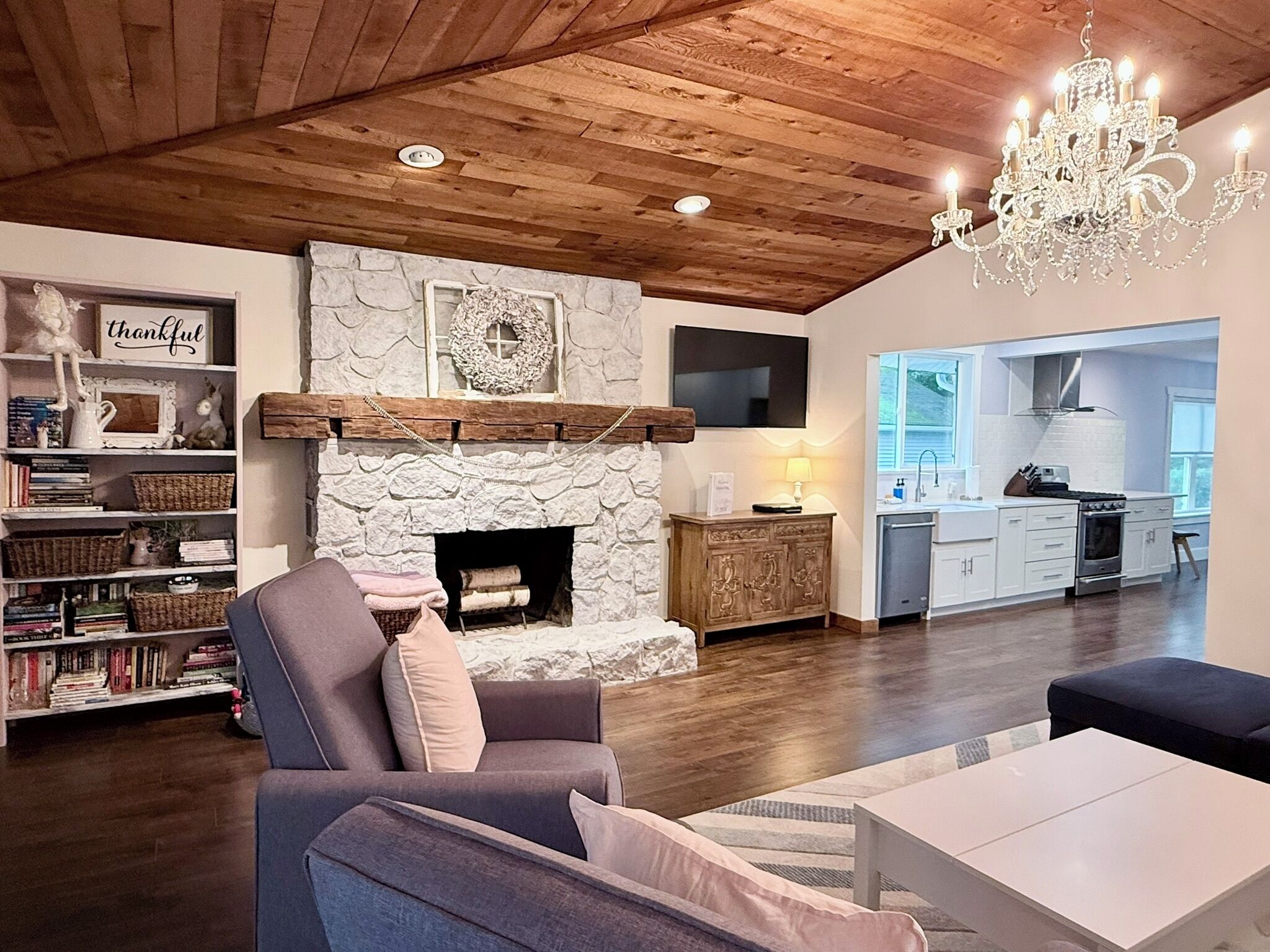 A living room with a stone fireplace, wooden ceiling, and a chandelier.