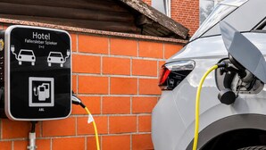 Estación de carga para vehículos eléctricos en un hotel, con pared de ladrillo al fondo y un coche aparcado conectado.