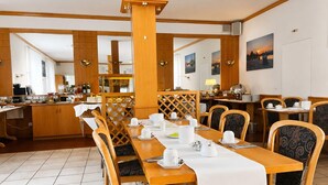 Comedor con mesas y sillas de madera, una cocina al fondo y vistas de la puesta de sol a través de las ventanas.