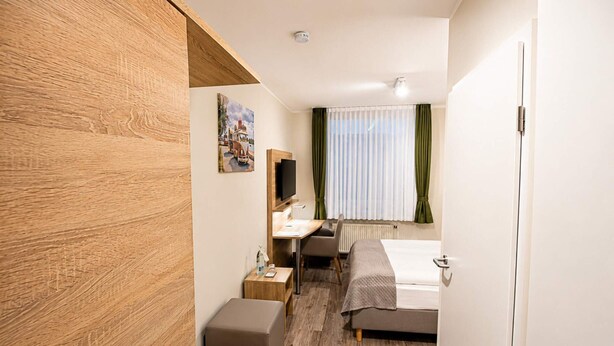 Habitación de hotel con pared de madera decorativa, una cama, un escritorio con silla, un televisor y una ventana con cortinas.