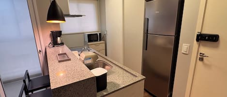 Una cocina compacta con una isla integrada, microondas, cafetera y refrigerador de acero inoxidable.