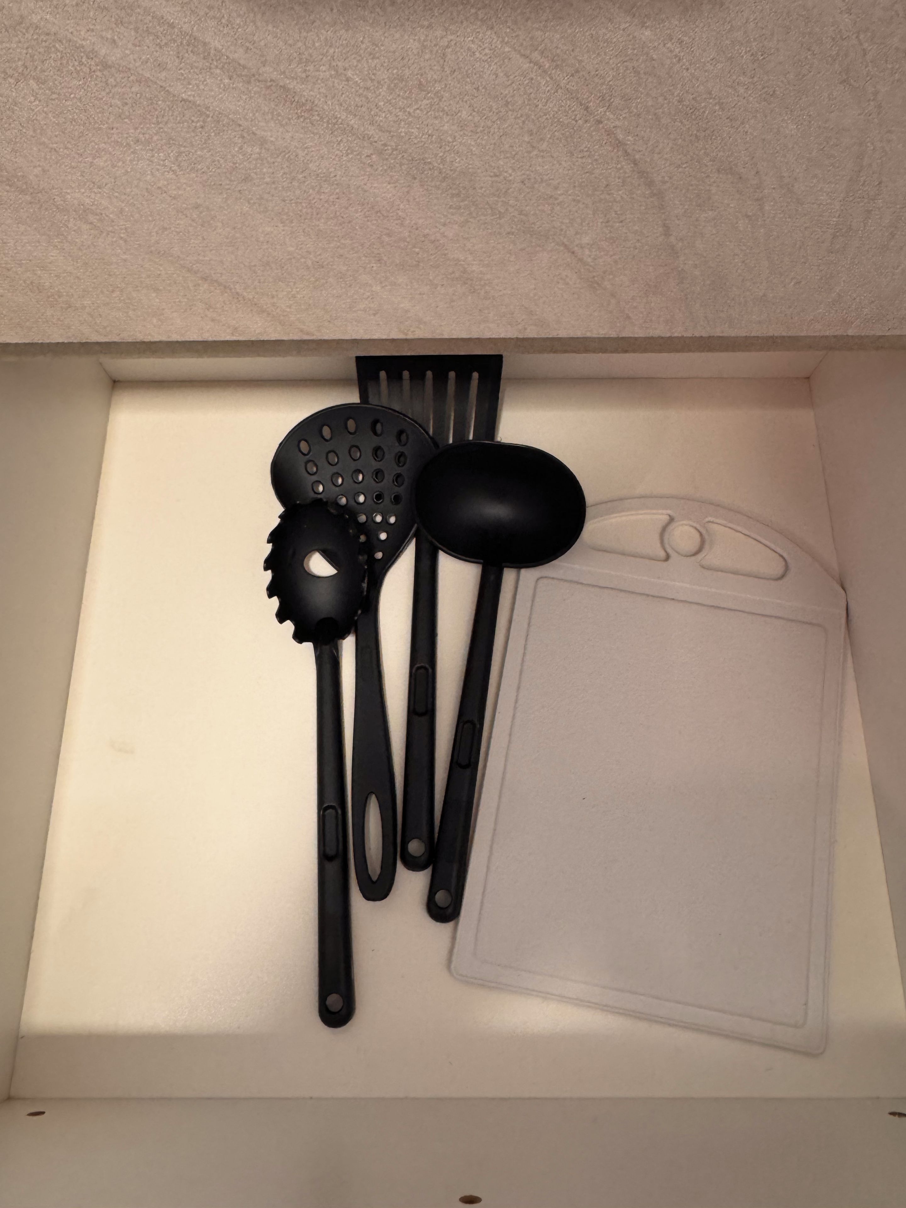 A kitchen drawer with various black kitchen utensils including spatulas, a ladle, and a strainer.