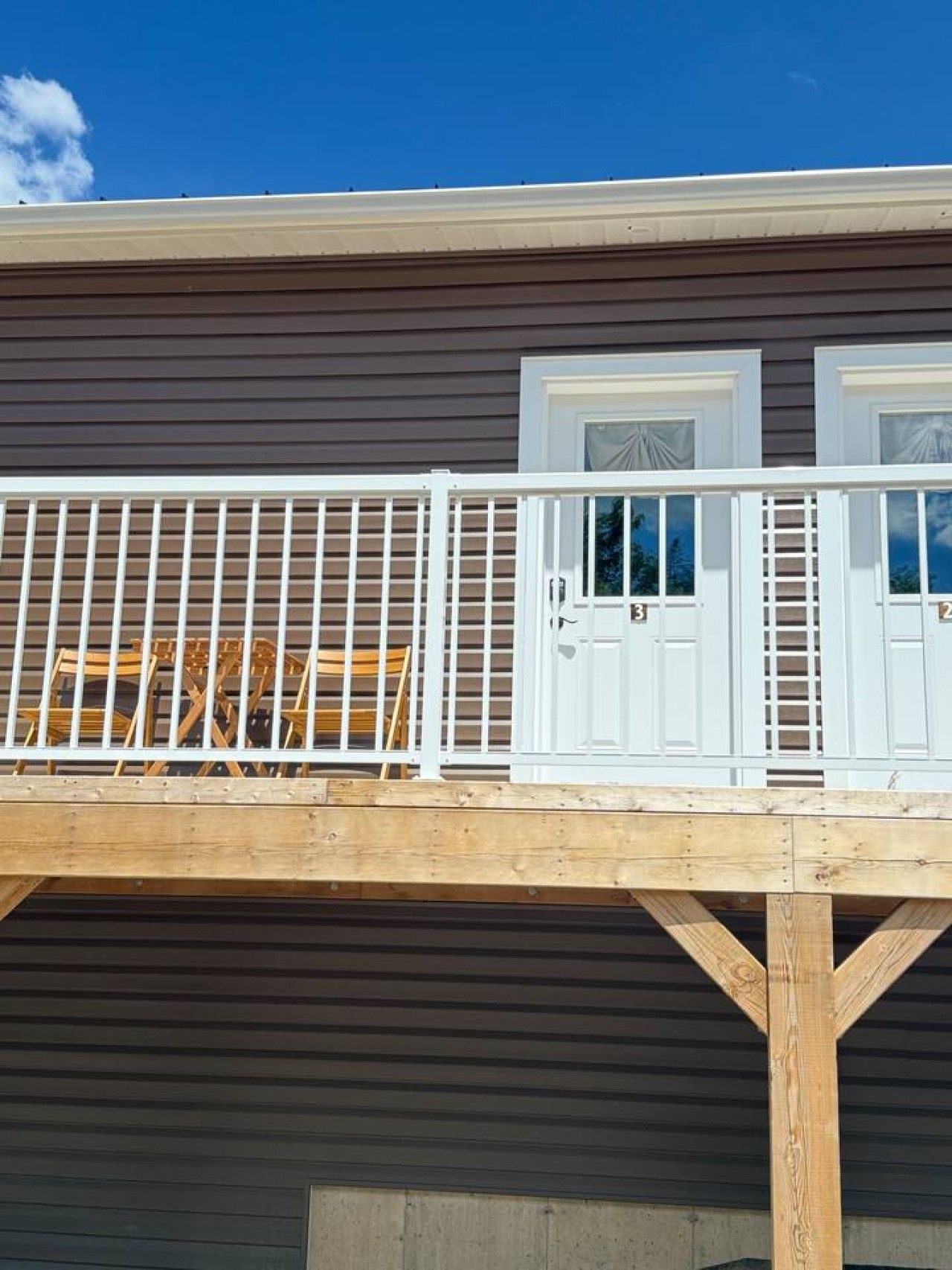 A wooden deck with a white railing, two doors, and a window with a view of the sky.