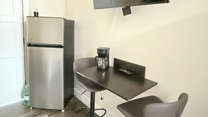 A kitchenette with a refrigerator, a coffee maker, and a flat-screen TV mounted on the wall.