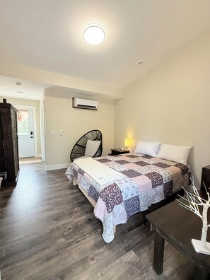 Un dormitorio con cama, una silla, una mesita de noche con lámpara y un banco de madera.