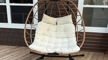 A wicker swing chair with cushions on a wooden deck.