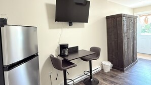 A compact kitchen with a refrigerator, a coffee maker, and a TV mounted on the wall.