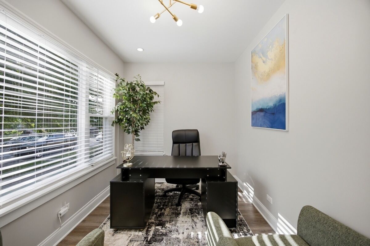 A modern office space with a black desk, a chair, a potted plant, and a painting on the wall.