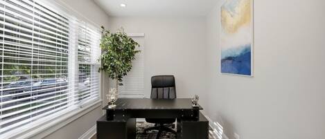 A modern office space with a black desk, a chair, a potted plant, and a painting on the wall.