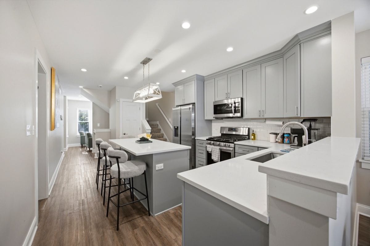 A modern kitchen with grey cabinets, stainless steel appliances, and a central island with bar stools.