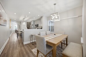 Uma cozinha moderna com armários brancos, uma ilha central e um espaço de refeições com mesa e cadeiras de madeira.