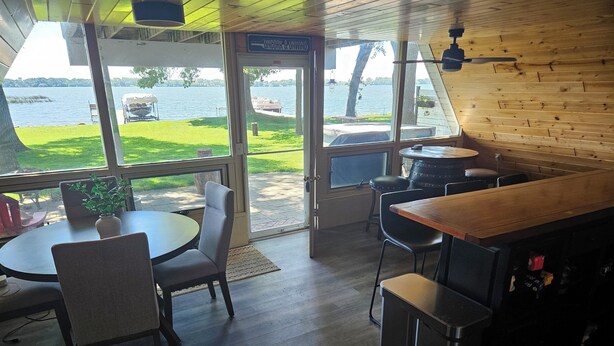 A room with a wooden ceiling, a round table with chairs, a bar area, and a view of a lake.
