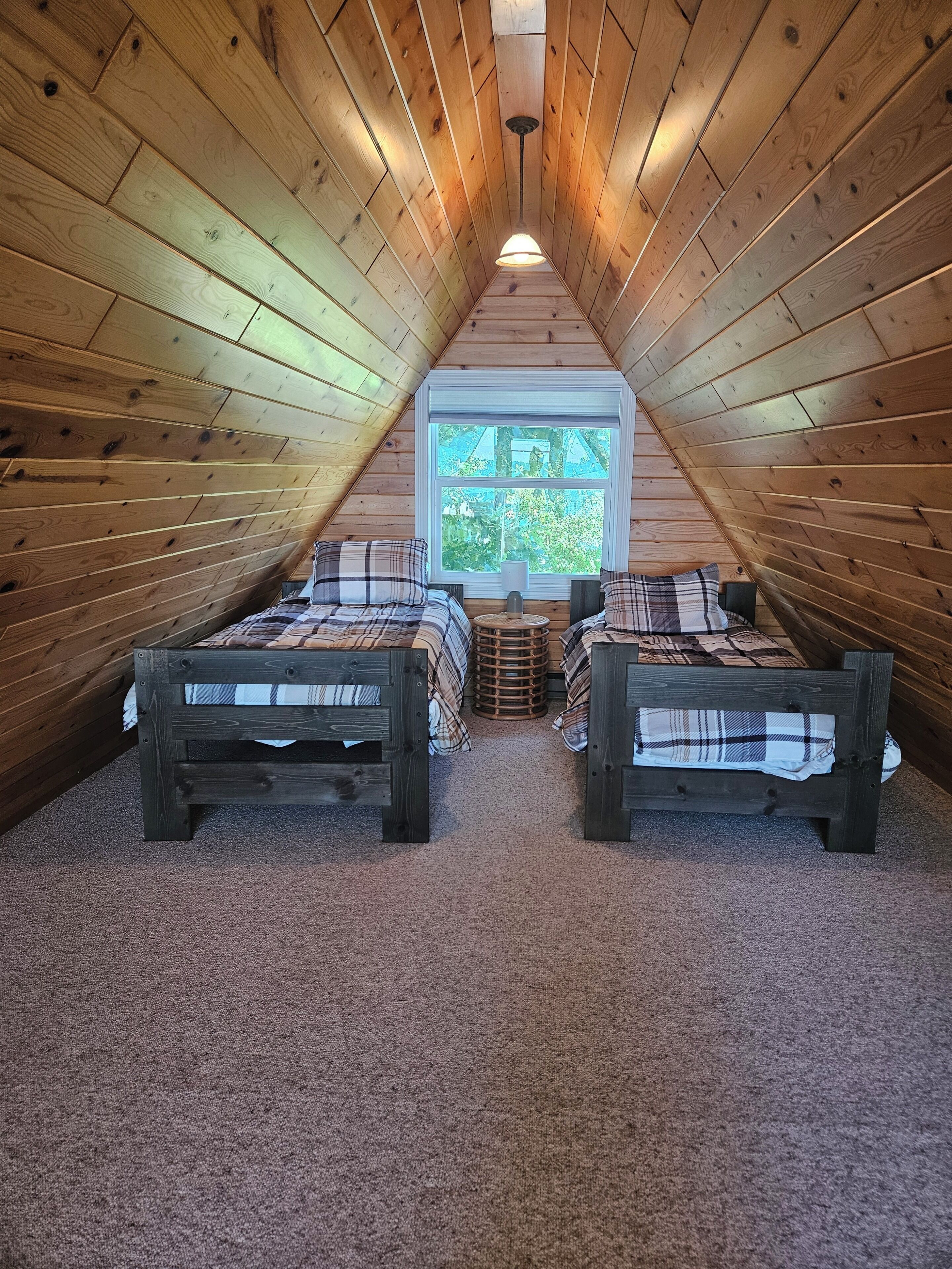 Une chambre mansardée chaleureuse, avec deux lits en bois, une fenêtre et un plafond en pente.