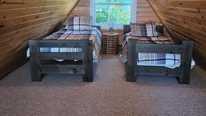 A cozy attic bedroom with two wooden beds, a window, and a sloped ceiling.