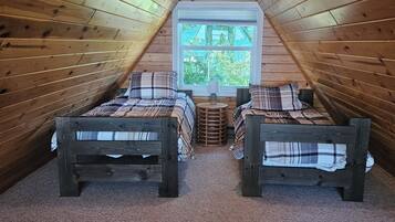 Une chambre mansardée chaleureuse, avec deux lits en bois, une fenêtre et un plafond en pente.