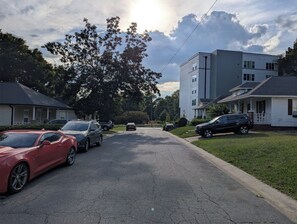 Rua residencial com carros estacionados, casas e um edifício alto.