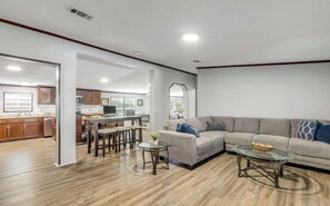 Ein geräumiges Wohnzimmer mit einem großen Sofa, einem Glastisch und einem Essbereich mit Holzzmöbeln.