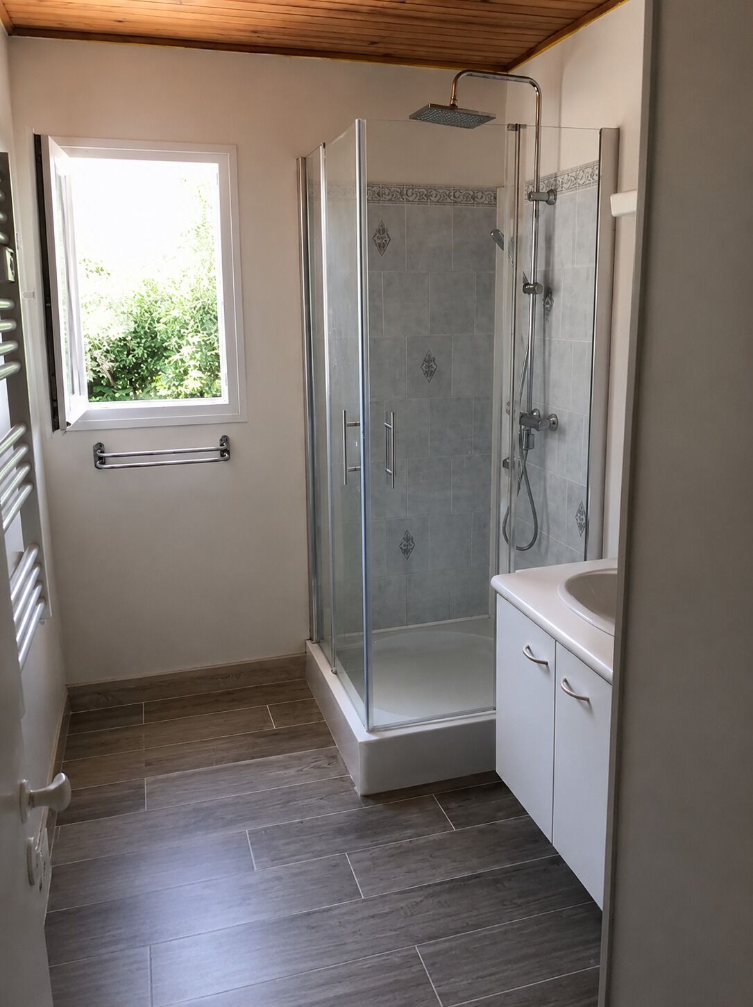 A bathroom with a glass-enclosed shower, a window, and a white sink.