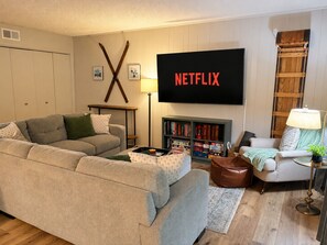 A living room with a sofa, a coffee table with board games, a bookshelf, a TV with 'NETFLIX' on the screen, and a lamp. - Lake Access, Game Room, Close to Skiing, Sleeps 10 (Albrightsville)