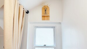 Een badkamer met een raam, een gordijn en een wandplank met decoratie.