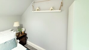 Een slaapkamer met een bed, nachtkastje, lamp en een plank met decoratieve objecten.