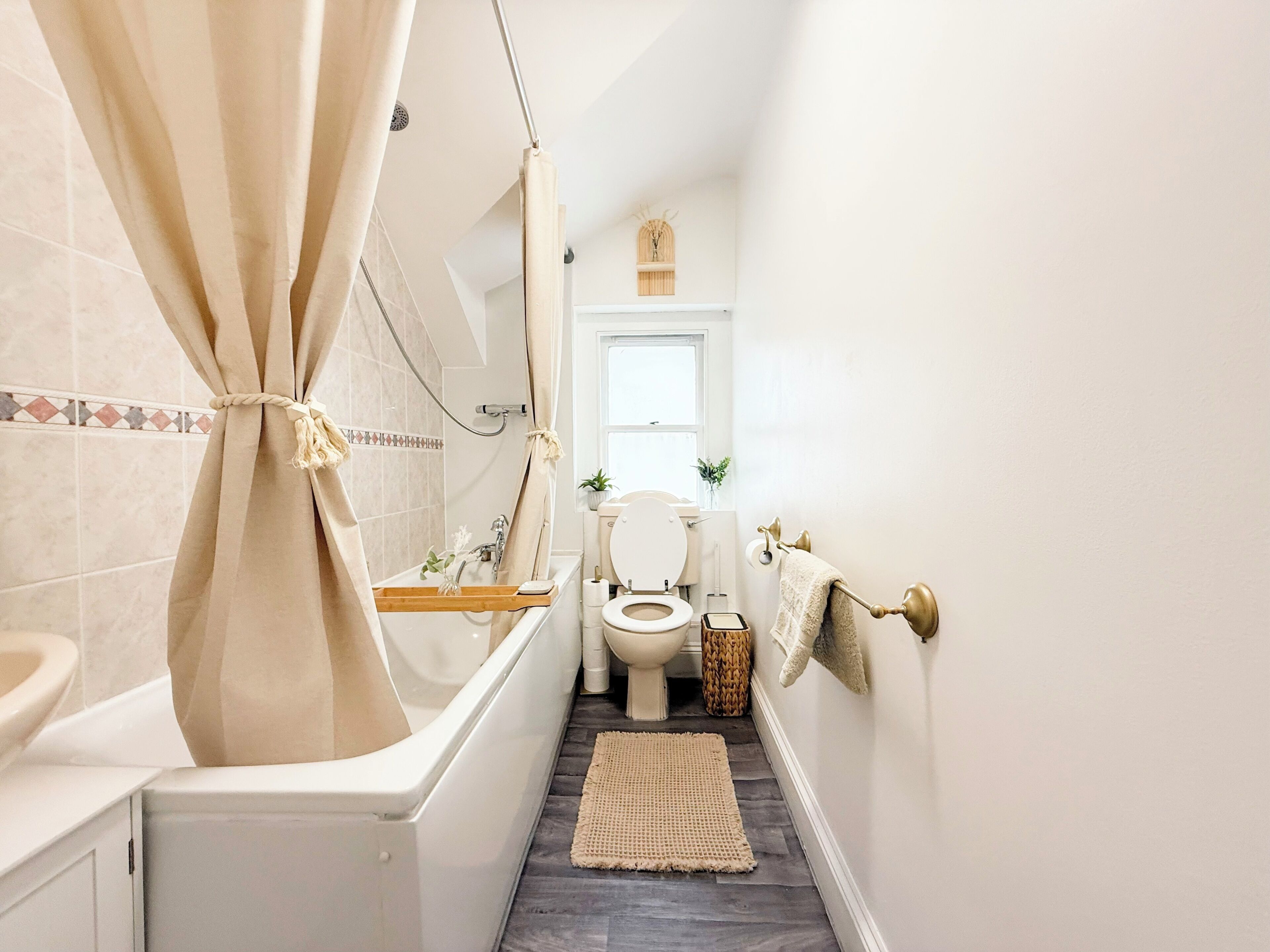 Ein schmales Badezimmer mit Badewanne, Toilette und Duschbereich.