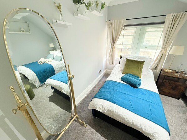 Une chambre d’hôtel avec deux lits, un grand miroir, une fenêtre avec des rideaux et une table de chevet avec une lampe.