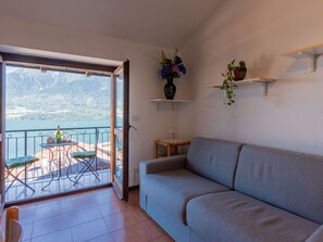 Una sala de estar con sofá, una mesa de comedor con sillas, un balcón con vista al mar y una planta en maceta sobre una repisa.