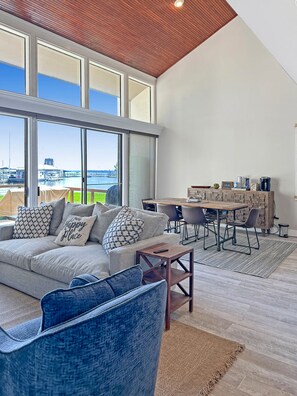 A spacious living room with a large window, a sofa, a coffee table, and a dining area with chairs and a table. - Lake Conroe, waterfront, boat dock, pets welcome (Montgomery)