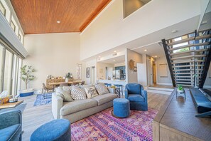 A spacious living area with a large sofa, ottoman, and blue armchairs. A kitchen is visible in the background, and a staircase leads to an upper level. - Lake Conroe Luxury Retreat - Boat Slip & Sunsets (Montgomery)