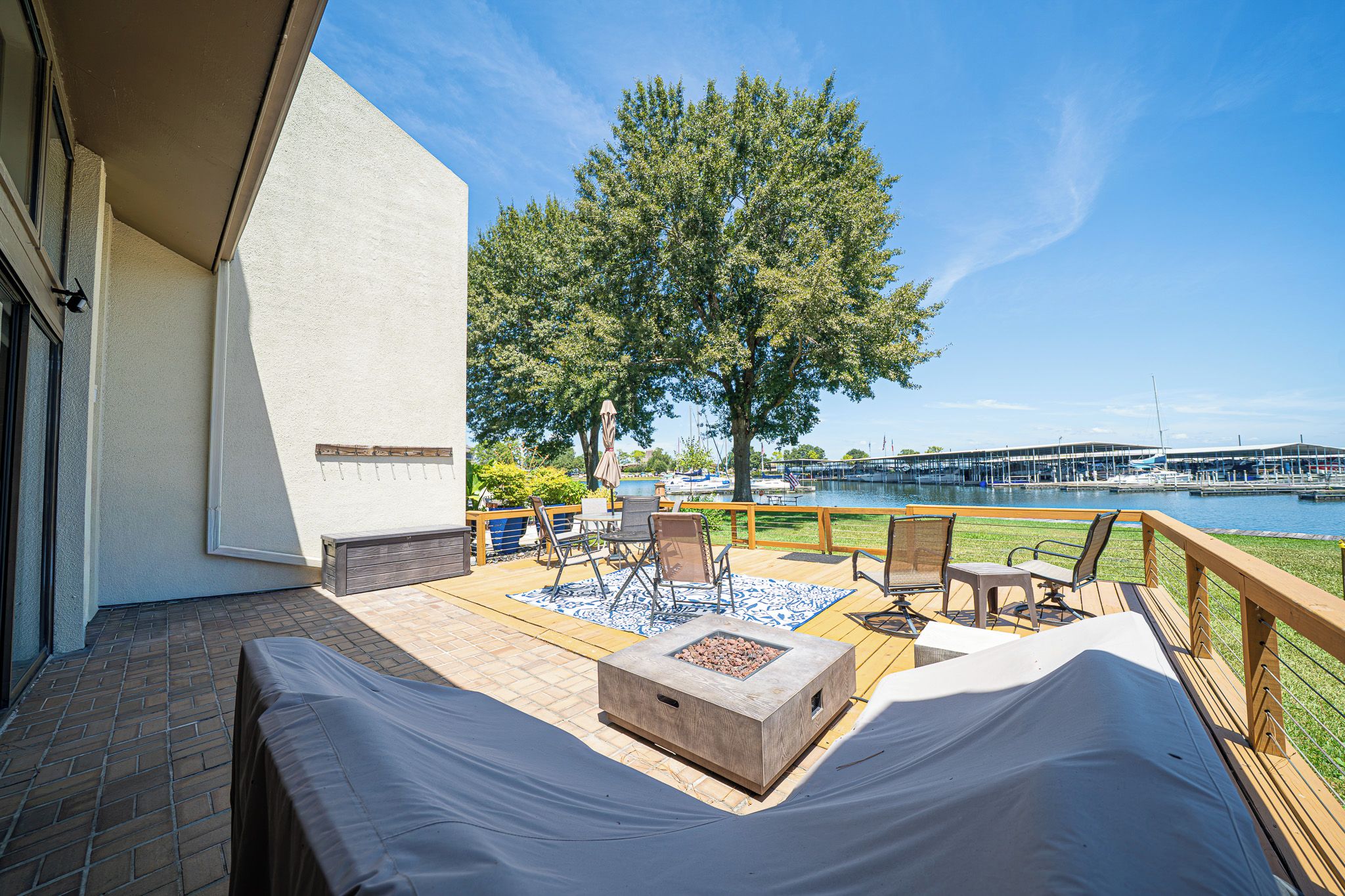 A covered outdoor seating area with a fire pit, chairs, and a view of a marina.